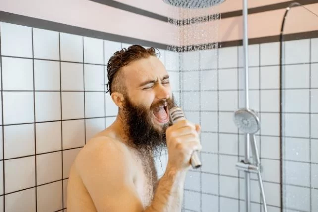 A bearded man is singing into a microphone while showering